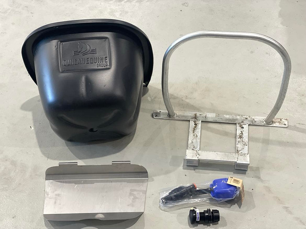 Collection of automotive parts including a black housing, metal bracket, and small components on a concrete surface.