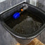 Black water tank with a blue float valve on a wooden floor.